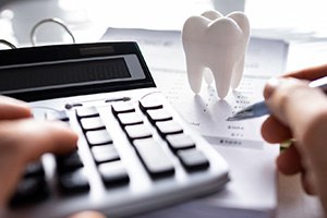 Hands holding pen and pressing calculator buttons at desk with invoice and large model tooth