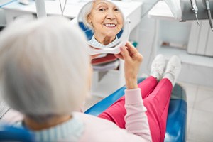 Senior woman sitting in dental chair checking smile in mirror