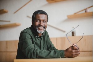 older man smiling and holding his glasses