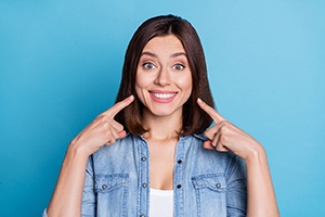 An adorable lady dressed denim shirt pointing fingers at her white teeth