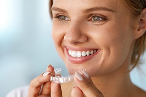 A smiling woman with white teeth holding a whitening tray
