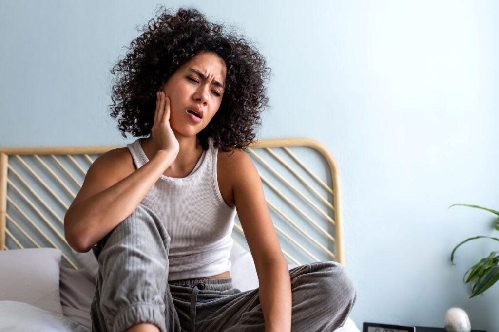 A woman sitting in bed holding her jaw from a toothache.