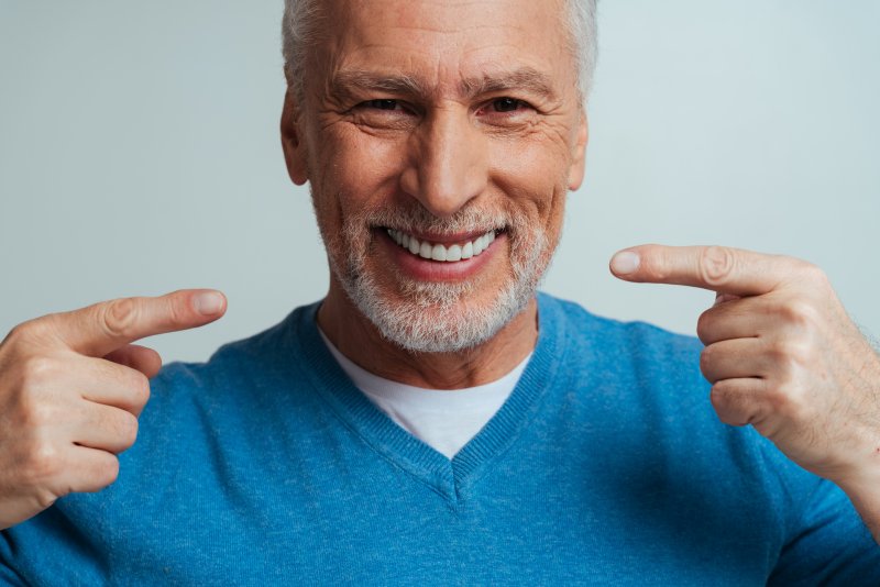 An older man pointing out his white and bright dentures